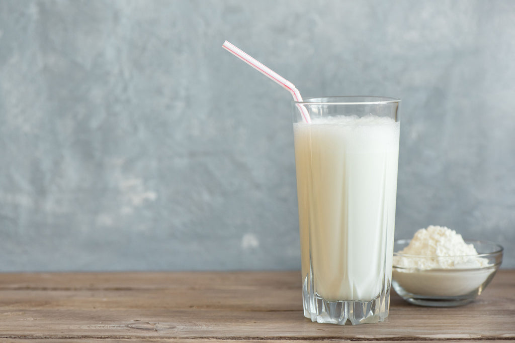 Glass of whey protein and scoop of protein powder on table.