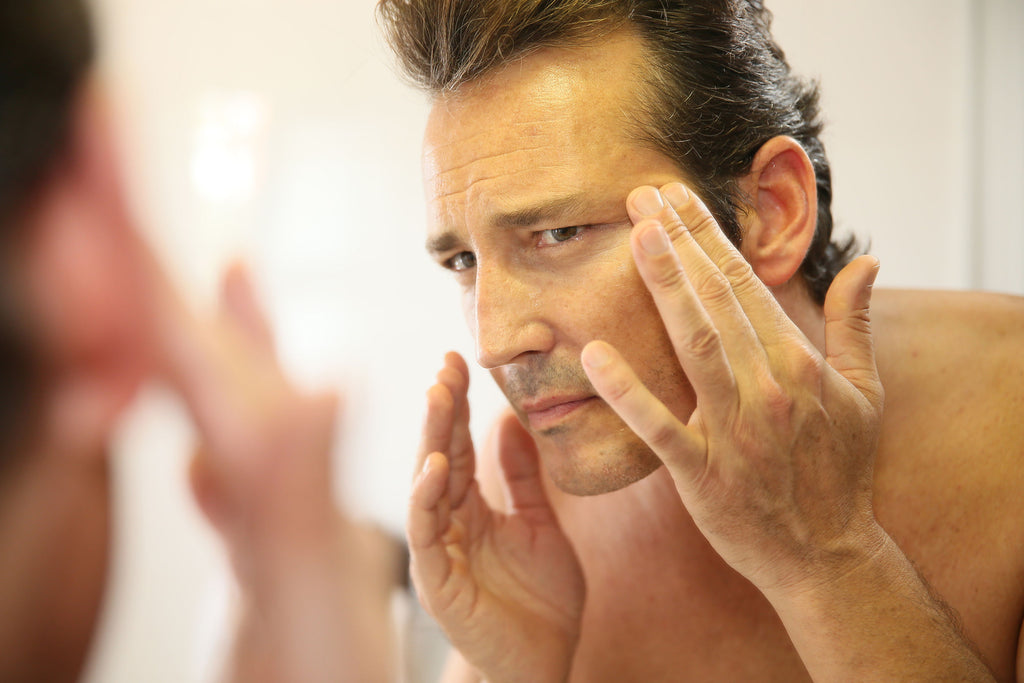 Middle-aged man looking into the mirror noticing wrinkles in his skin
