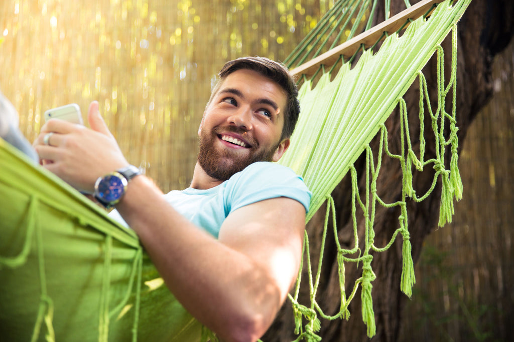 Man resting on hammock with smart phone in hand.