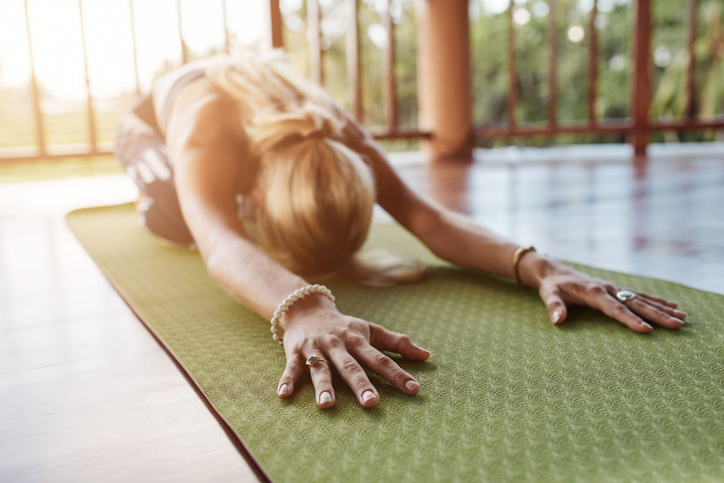 Woman stretching on a green yoga mat with the sun shining in the background