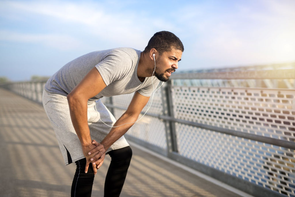 Man taking a break from a run places his hands on his knee