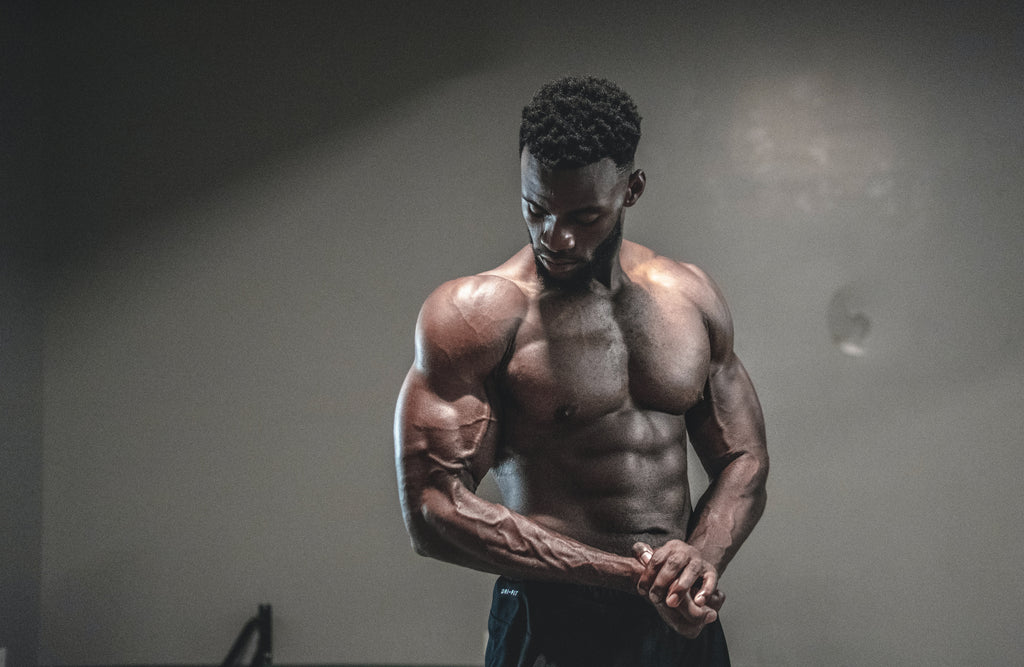 A muscular man flexing his arms and checking out his progress in a dark studio