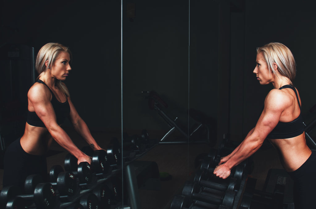 Fit woman standing in front of mirror with dumbbells ready to tackle a workout